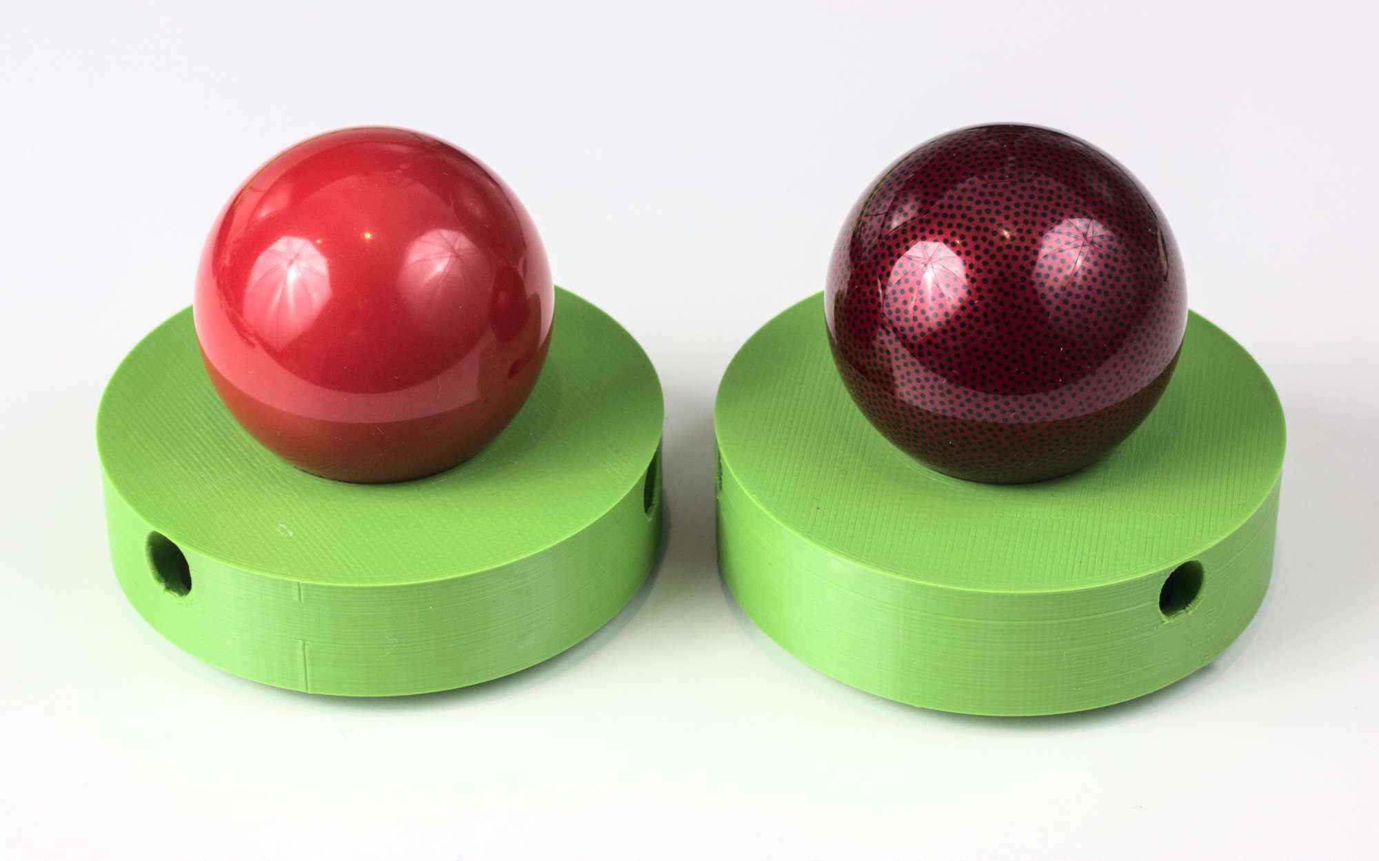 Polished pool ball next to slightly shinier ball. Both red.
