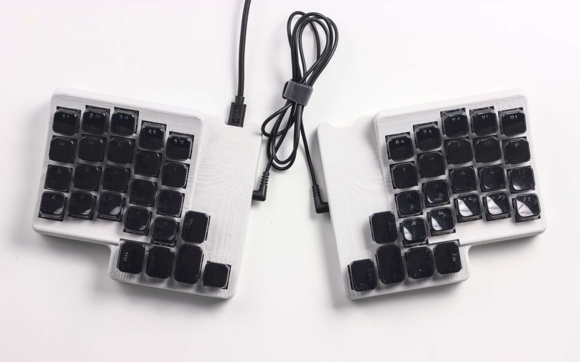 Keyboard with two halves joined by a small cable. Each half has a light grey base and black keys
