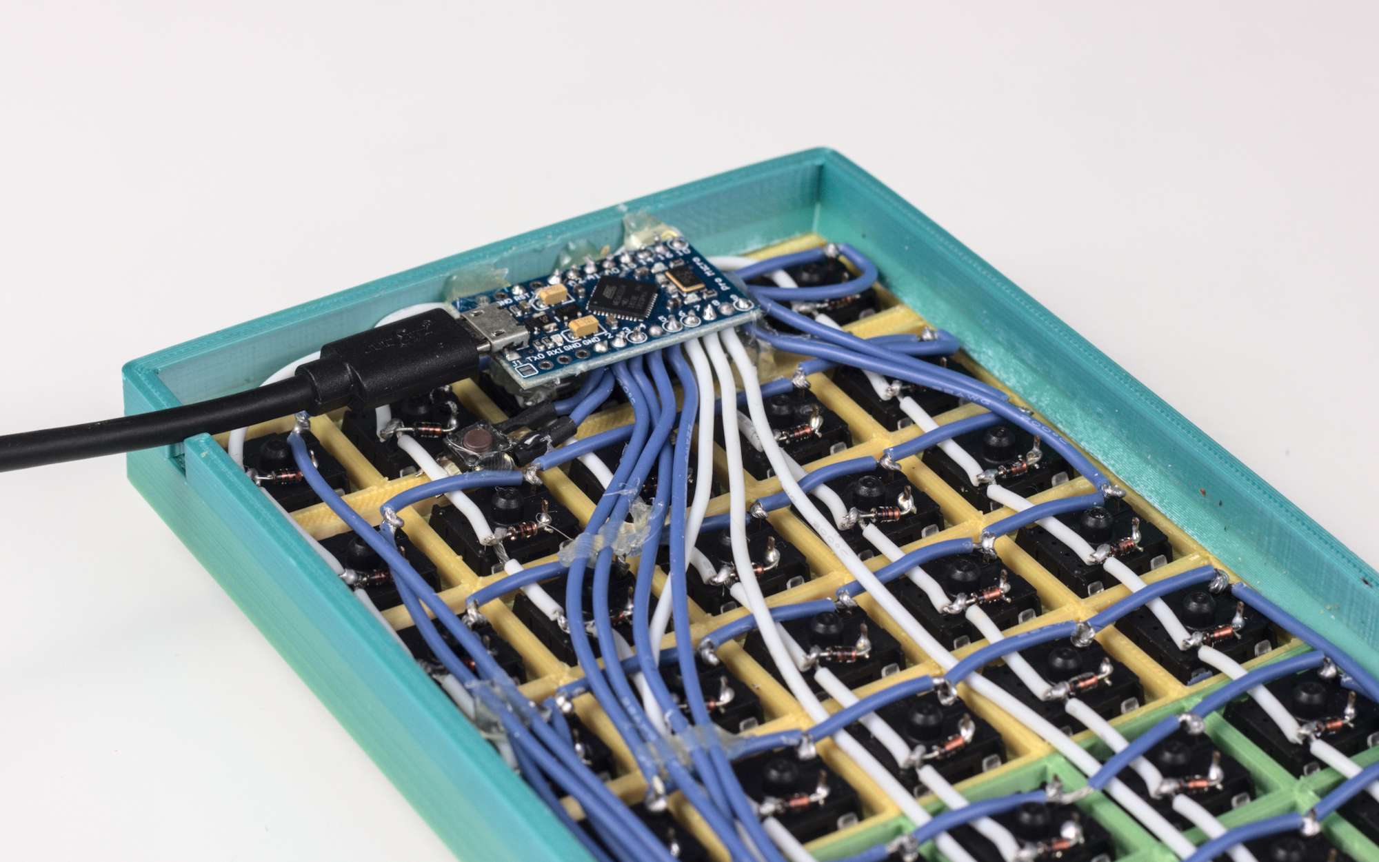 Close-up of hand-wired underside of keyboard, showing Arduino hot glued in place Close-up of hand-wired underside of keyboard, showing Arduino hot glued in place