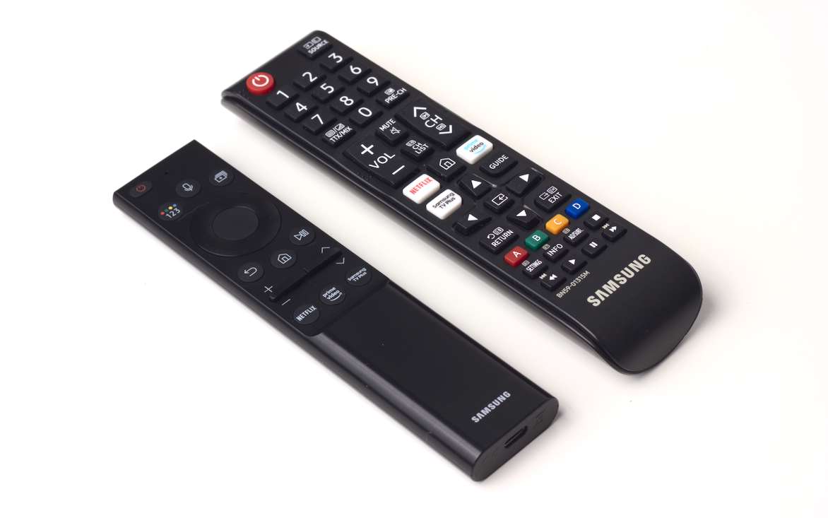 A sleek, minimal black metal remote next to a larger remote covered in colourful cheap silicone buttons.