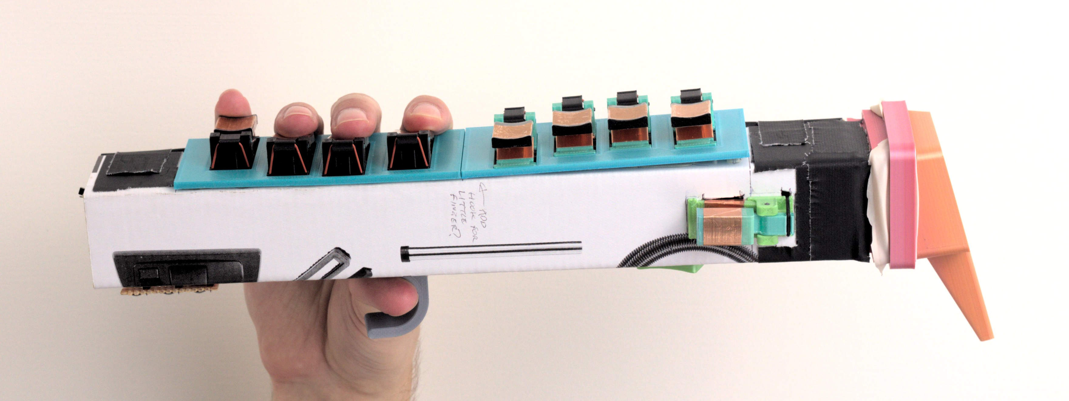 Another boxy cardboard prototype, with hybrid capacitive keys mounted to 3D printed plates all round it, and a mouthpiece on one end. Each key is a little see-saw lever that your finger presses one side of, with a rubber o-ring on the other side pulling it back up. The finger pads and part below them are wrapped in copper tape for conductivity.