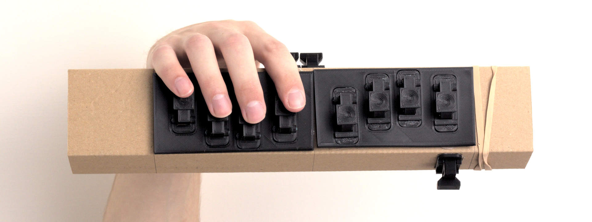 Long cardboard rectangular tube with 3D printed plates attached to the front. Each plate has 4 microswitch based keys on it. The keys each have a nice dished place to put your finger.