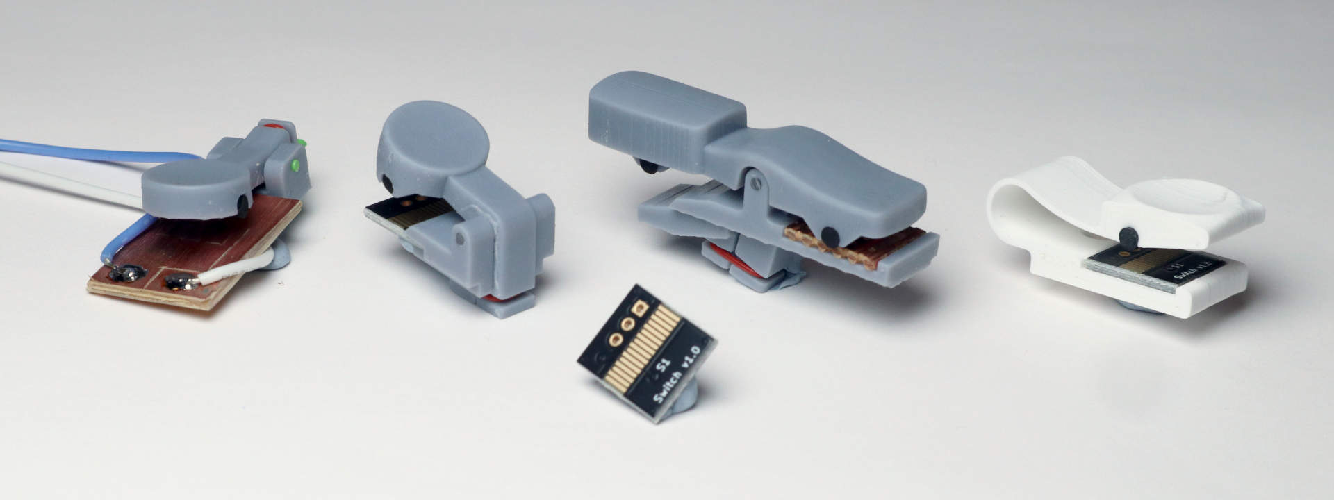 Lineup of keys using conductive silicone. Key 1 presses the silicone against a piece of copper-clad board. The remaining ones have a custom-made PCB which is shown in front of them. Keys 2 and 3 are resin printed designs - a finger key and a side key. Key 4 is a single-piece FDM print which uses a flexure to bend instead of a hinge and a rubber band.